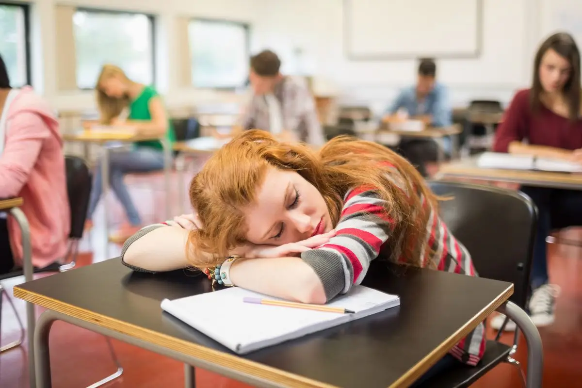 A tired female student resting on study table in classroom - Planning of Westchester